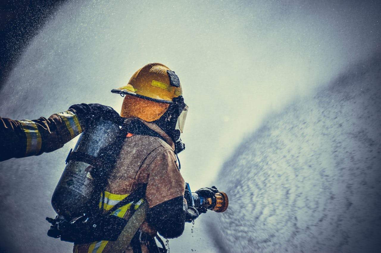 services-01 A brave firefighter in protective gear sprays water during training or emergency.